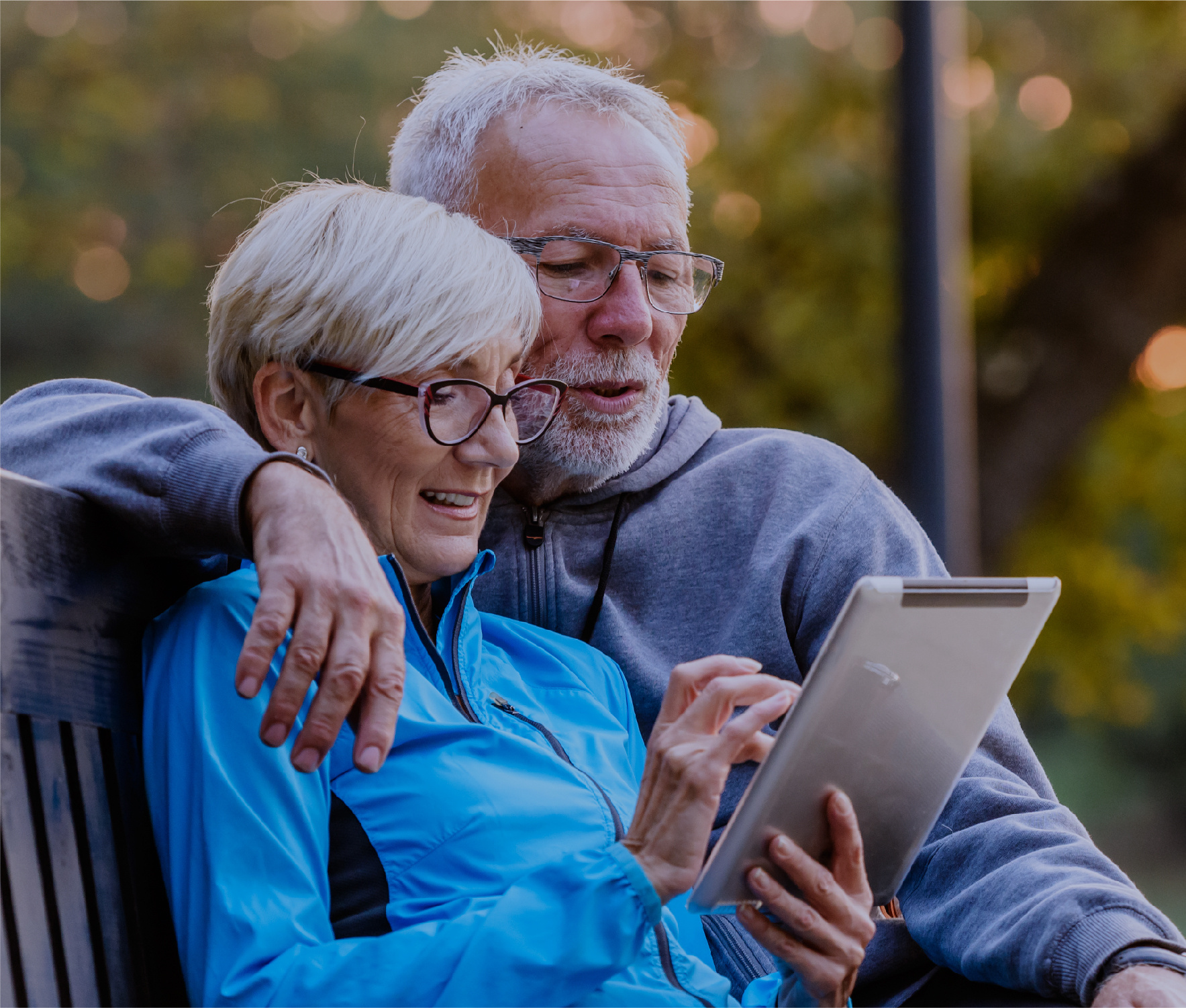 Mature couple sitting on bench looking at tablet